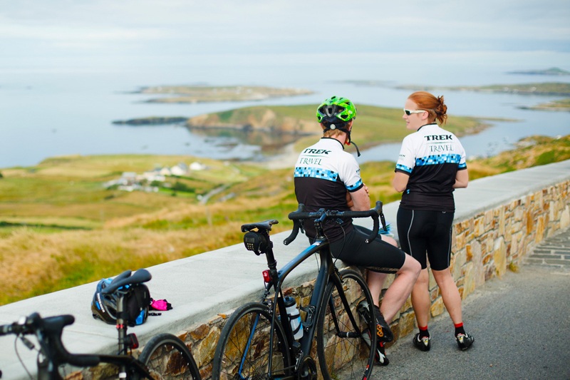 2 cyclists resting against a wall enjoying view of the Irish coast