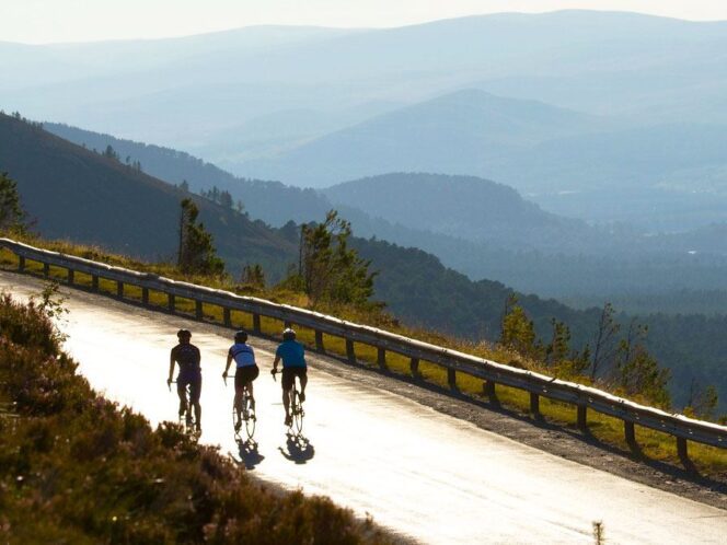 3 cyclists on a road against a mountainous backdrop