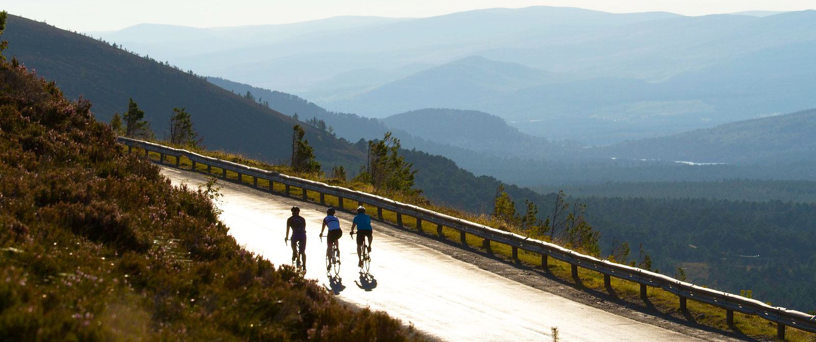 3 cyclists on a road against a mountainous backdrop