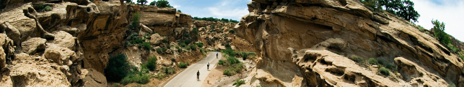 cyclists riding on a paved road through a rock wall pass