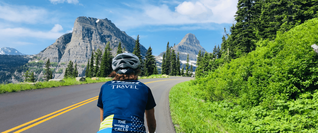back of a person riding their bike on a paved road with mountains in the background