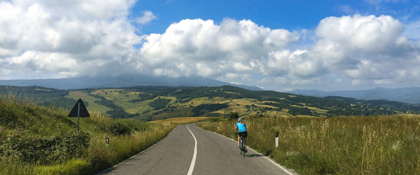 Cyclist heads downhill on road winding towards patchwork hills