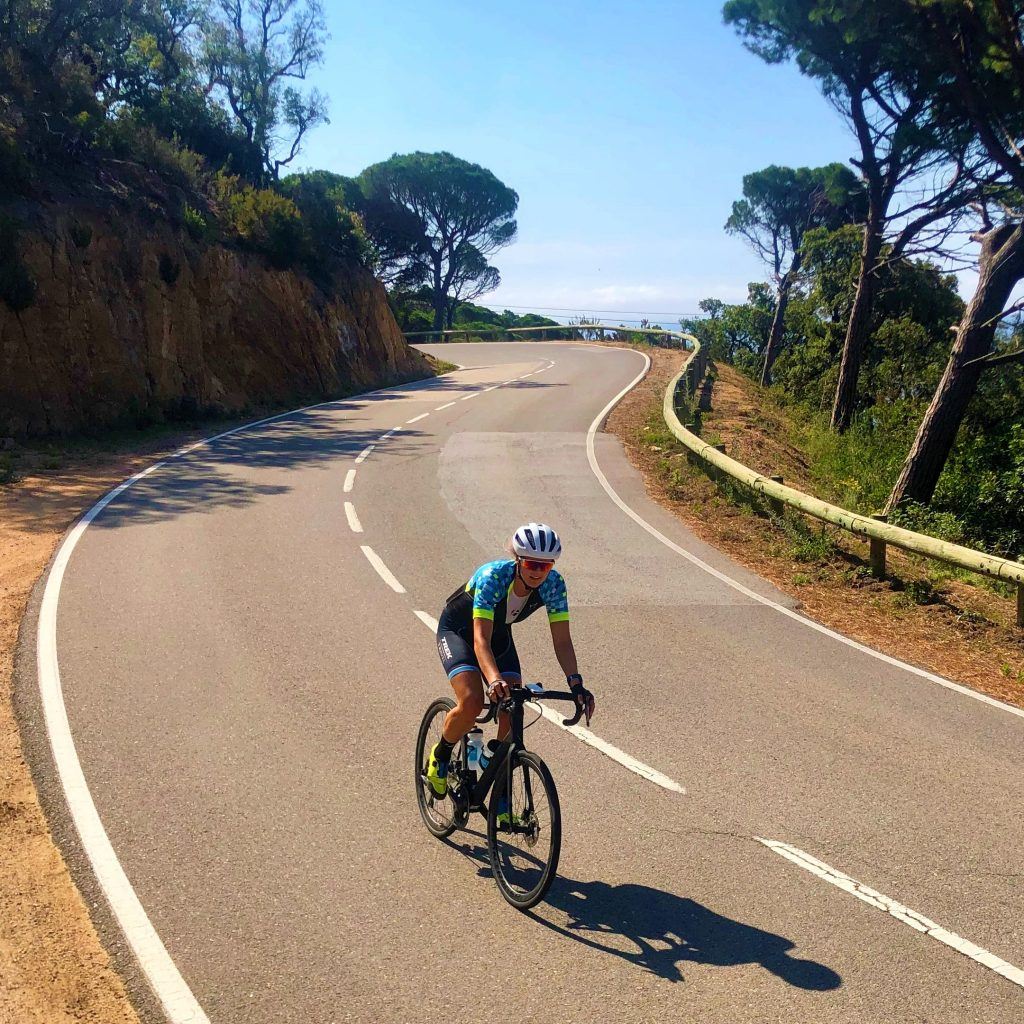 A cyclist cruises down a windinding road. It's a sunny afternoon without a cloud in the sky. The ocean is barely visible past the curve of the road.