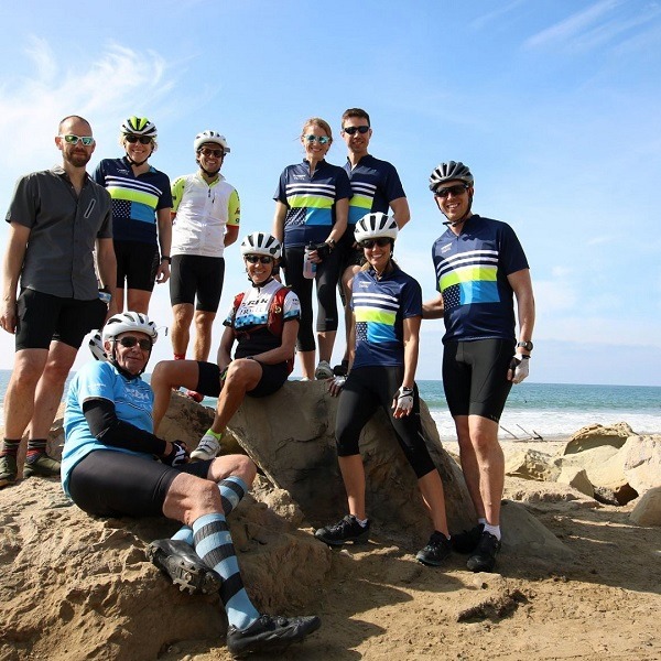 group of cyclist at the beach posing for a photo with the sea in the background