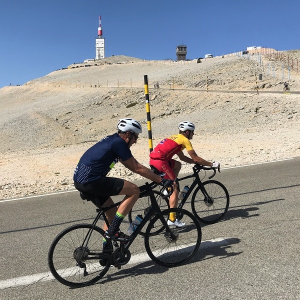 two people riding uphill with the antenna of the Mount ventoux in the background