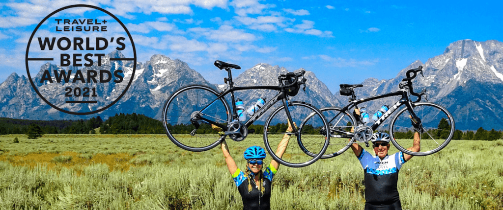 two people hoisting their bikes in the air with mountains in the background