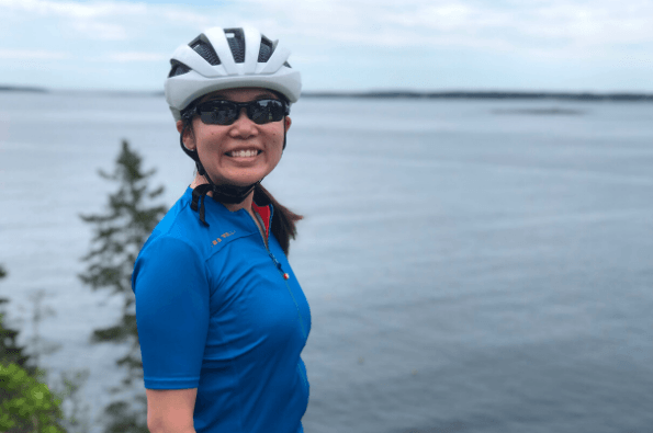 A person wearing a cycling helmet smiles as her photo is taken with Lake Menona of Wisconsin in the background