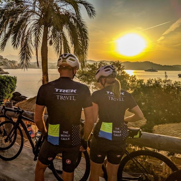 two cyclists resting in front of a California sunset with a palm tree framing the left side of the photo