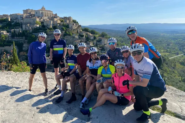 11 people with bike gear posing in front of a landscape with a village on a cliff
