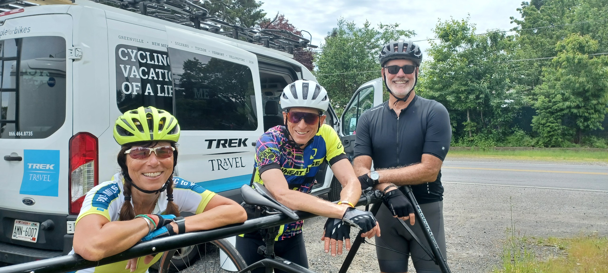 Three cyclists smiling and leaning on bike rack in front of Trek Travel van