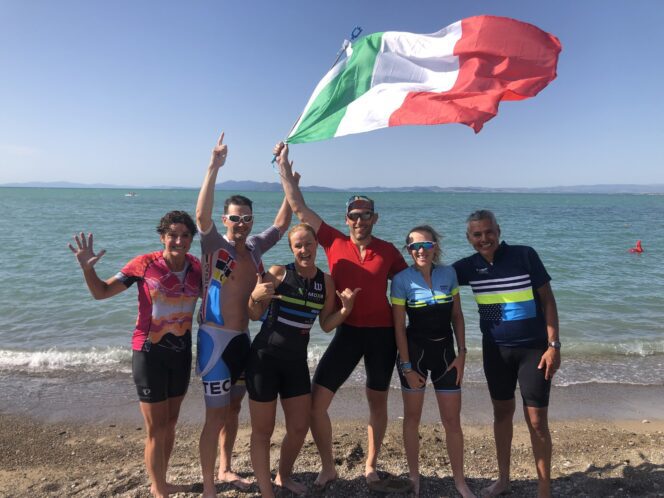 Cyclists in bike jerseys posing with the Italian flag on the beach.