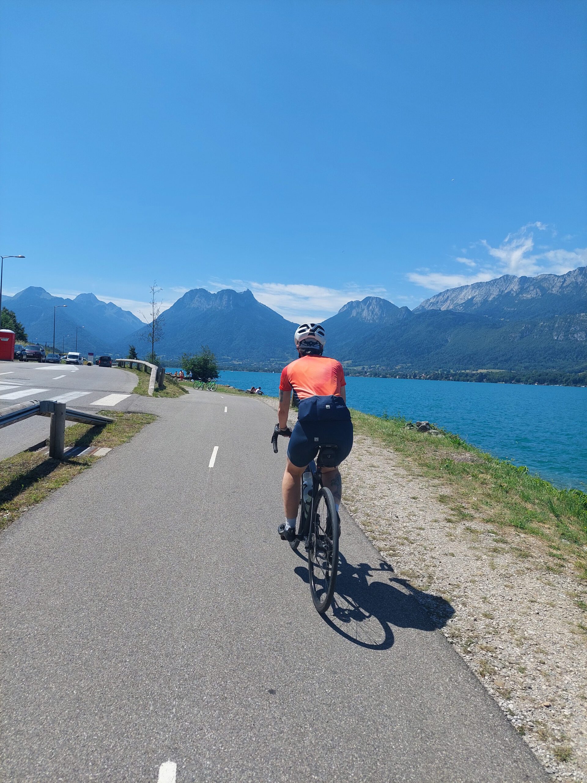 A person riding a bike from the back next to the lake of Annecy