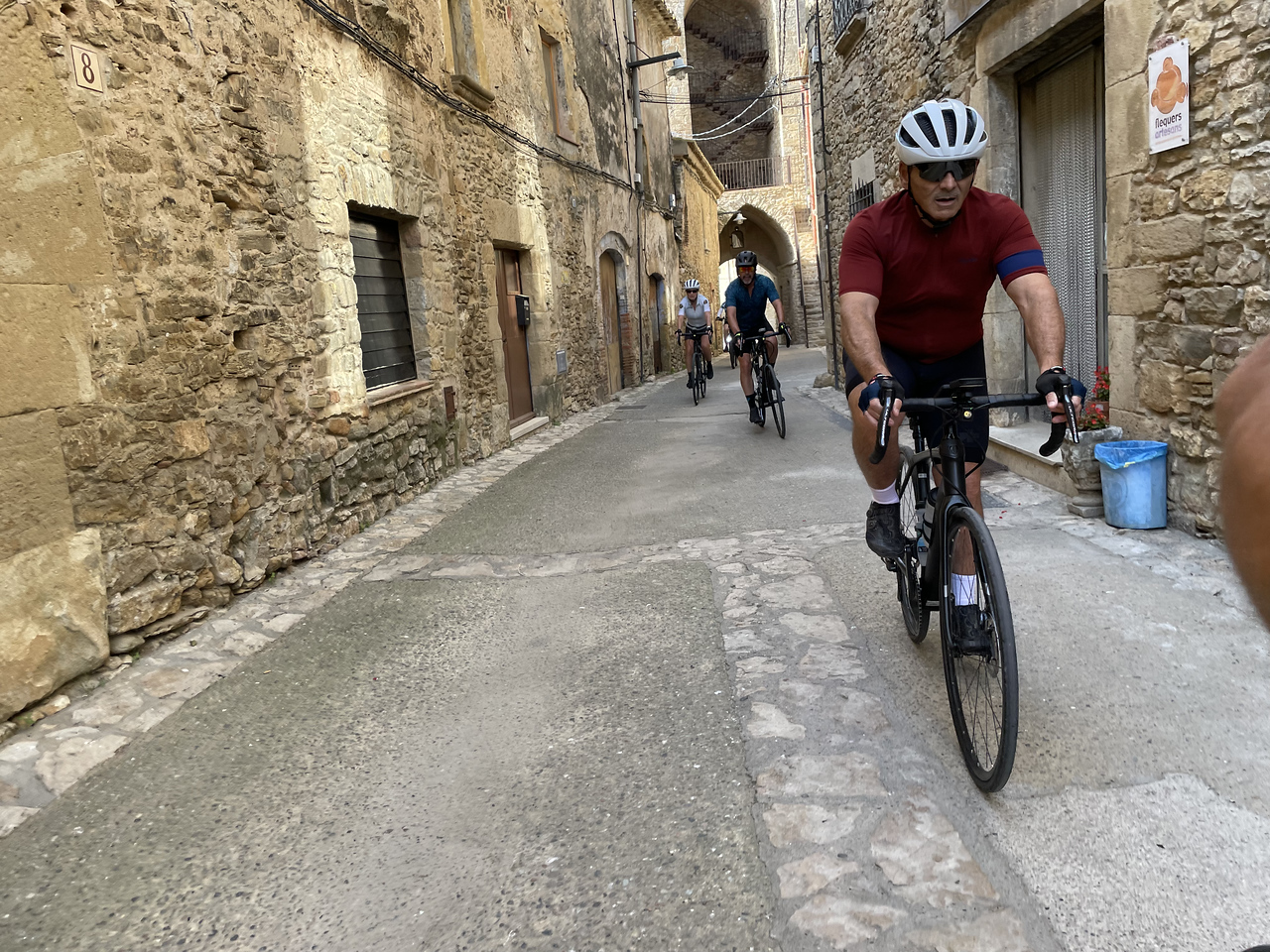 group of cyclists riding in a line through the old buildings of Girona's Old Town