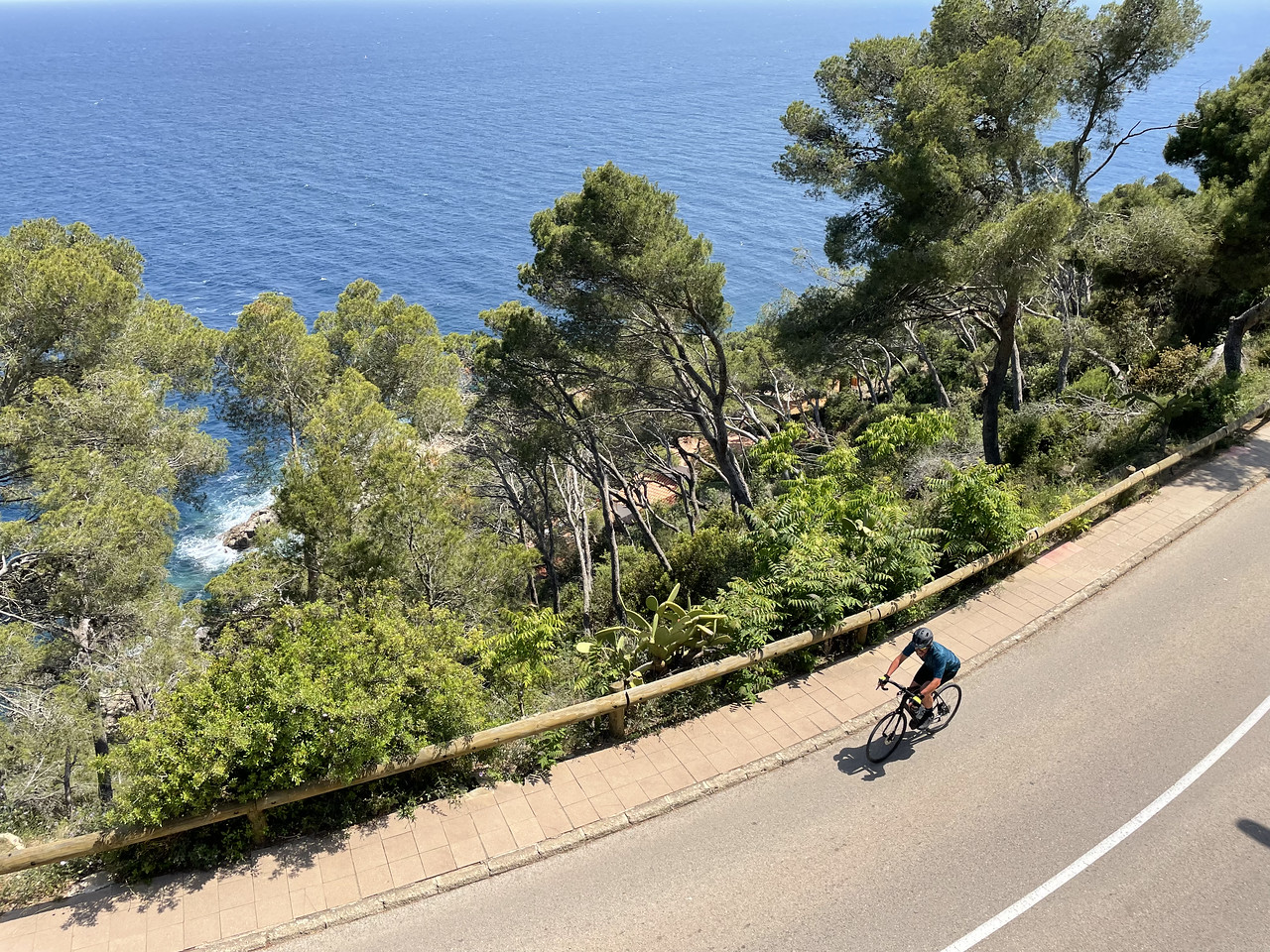 overhead photo of a single cyclist along the coast of Girona overlooking the sea