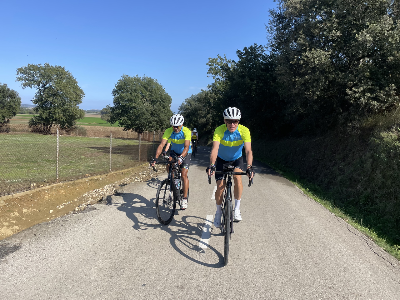two cyclists riding together, looking at the camera along a flat section of a route near Girona, Spain