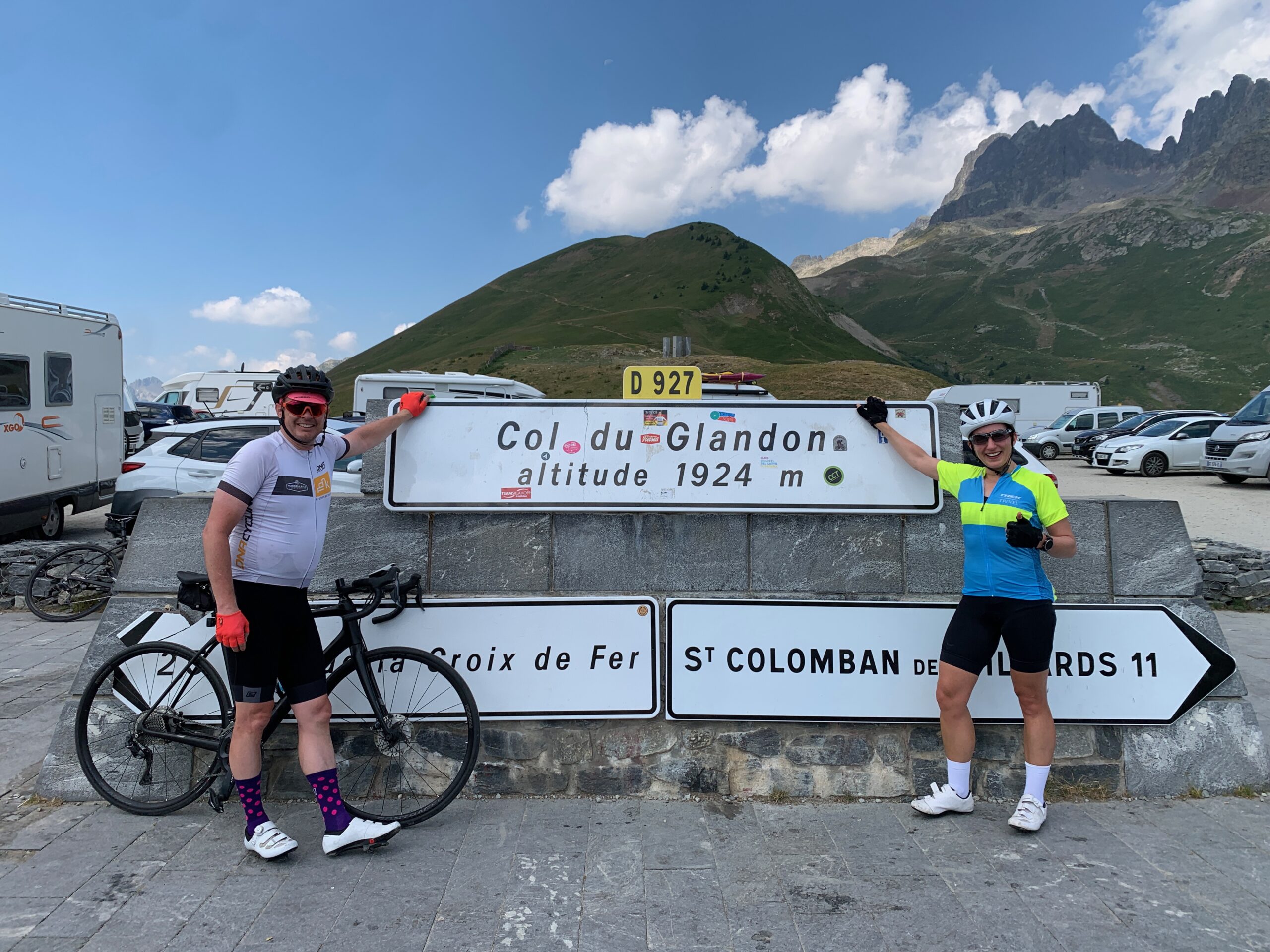 Two people standing on each side of the Col du Glandon sign