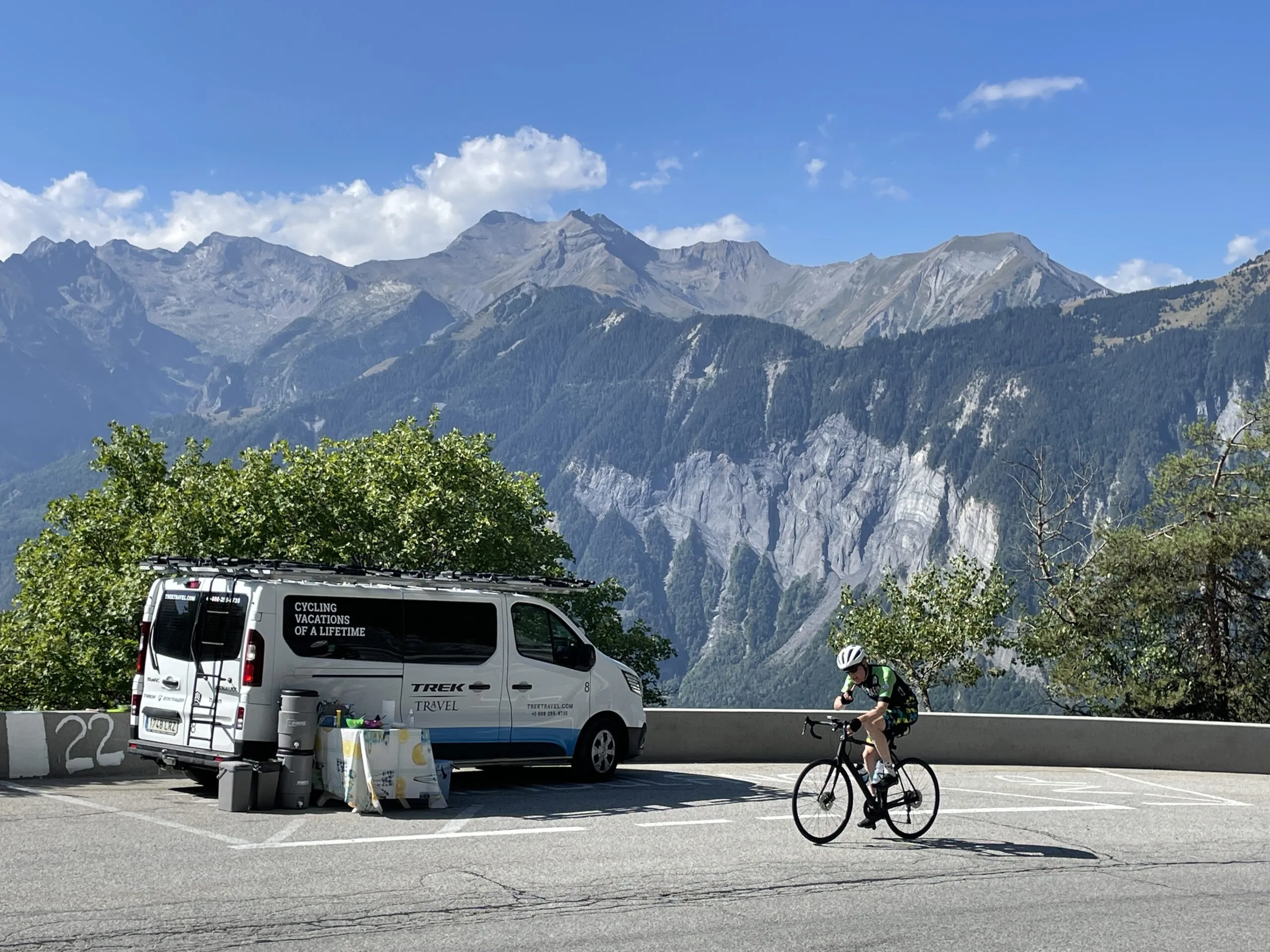 A person riding up to Alpe d'Huez next to the TT van with mountains in the background