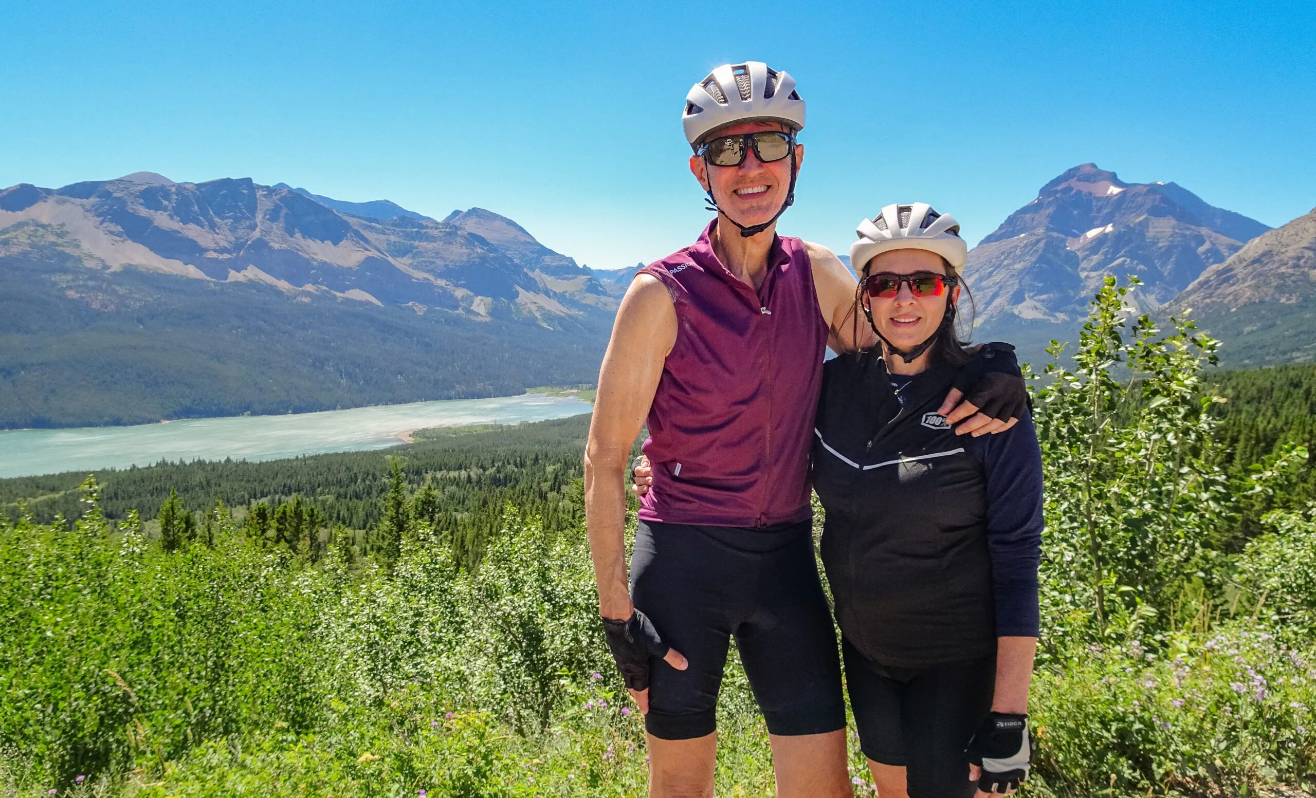 A couple pose in front of an elevated view of a lake and mountains