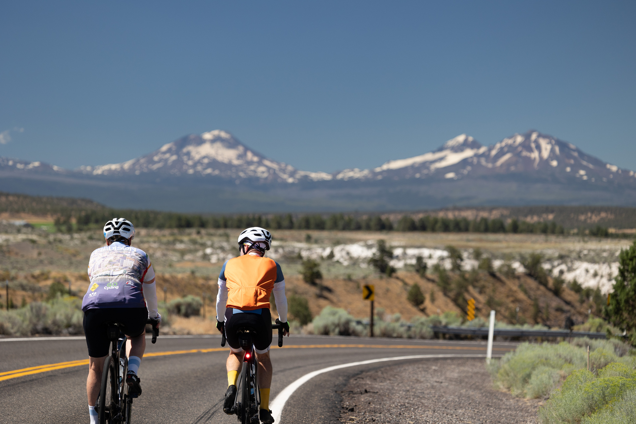 Two cyclists riding in Oregon with the Sisters Volcanos in the background