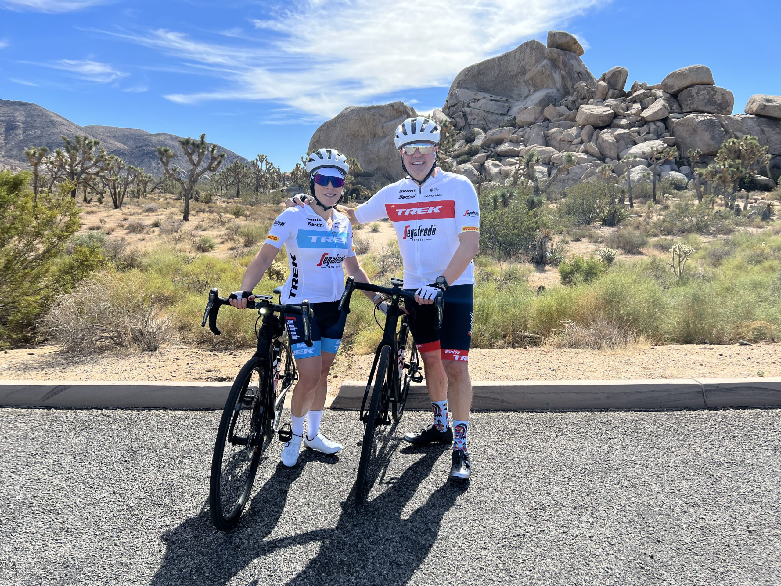 A couple pose with their bikes in front of cactus and rock formations