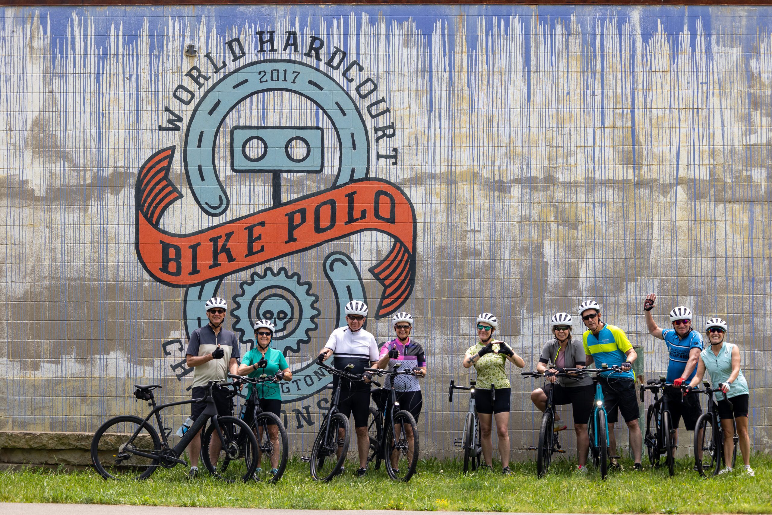 A group of cyclists pose in front of a wall mural