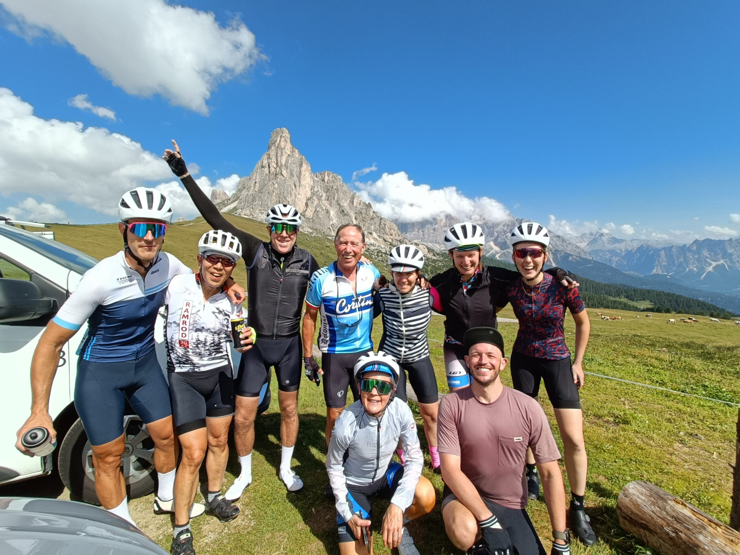 A group of cyclists pose and smile with mountain peaks in the background