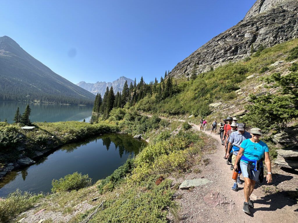 A row of hikers walking on a lakeside trail