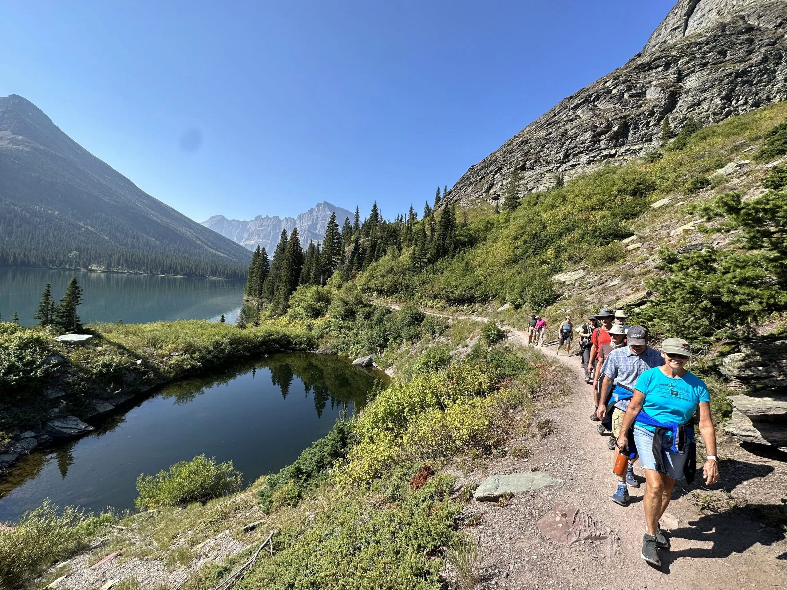 A row of hikers walking on a lakeside trail