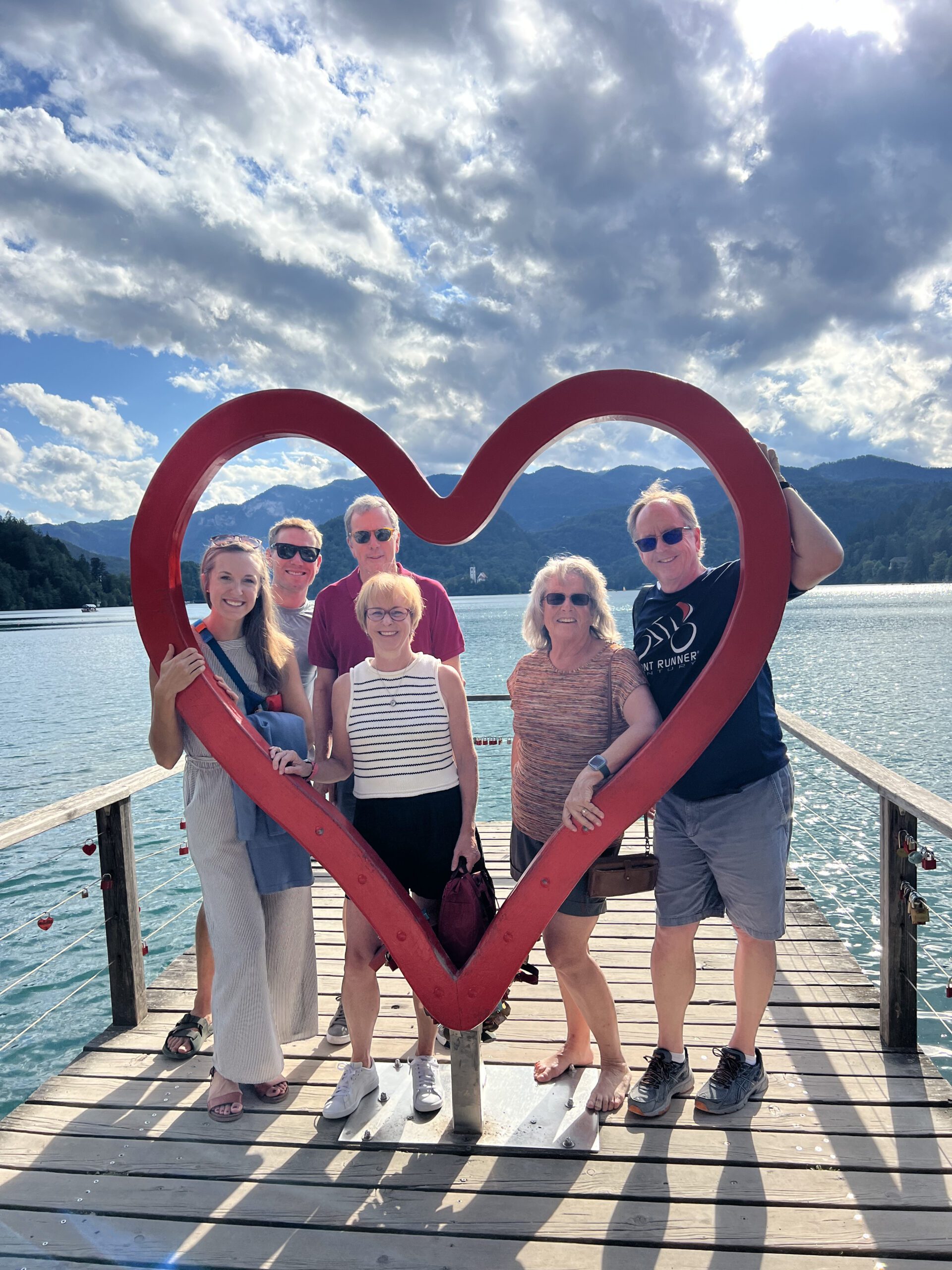 A group poses in a heart sculpture by a lake