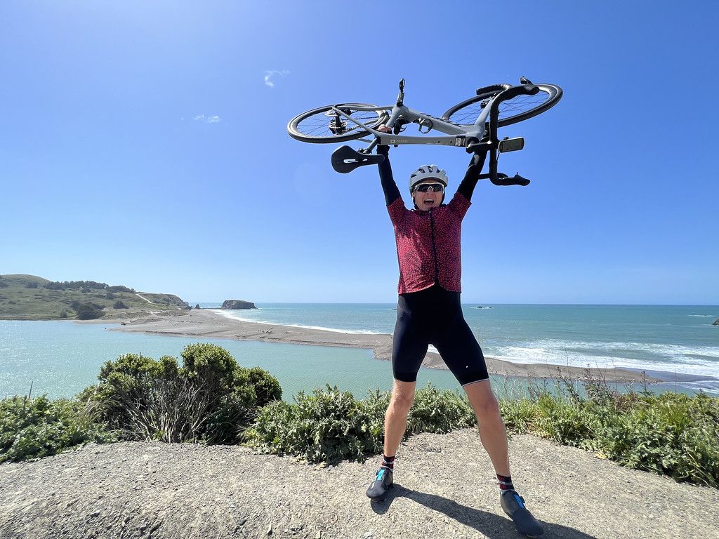 celebration shot holding bike over head in front of ocean