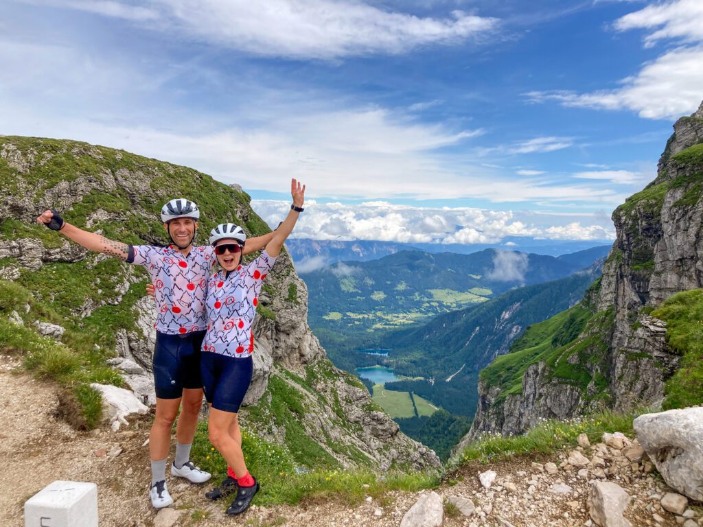 A happy couple in front of a scenic view of cliff rocks with lakes and mountains in the distance below