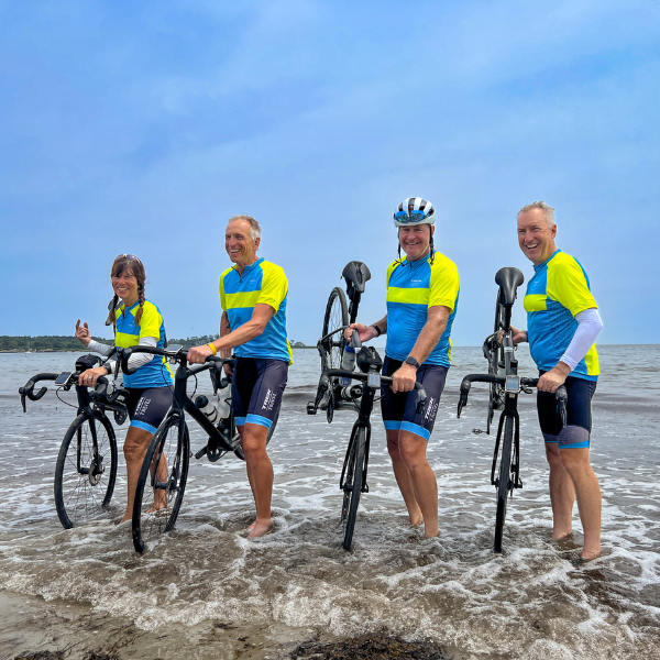 Four cyclists dipping their bikes in the Atlantic Ocean signifying their accomplishment of having ridden across the US
