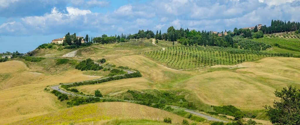 Rolling wheat fields, winding road, and houses on the hill tops in Tuscany