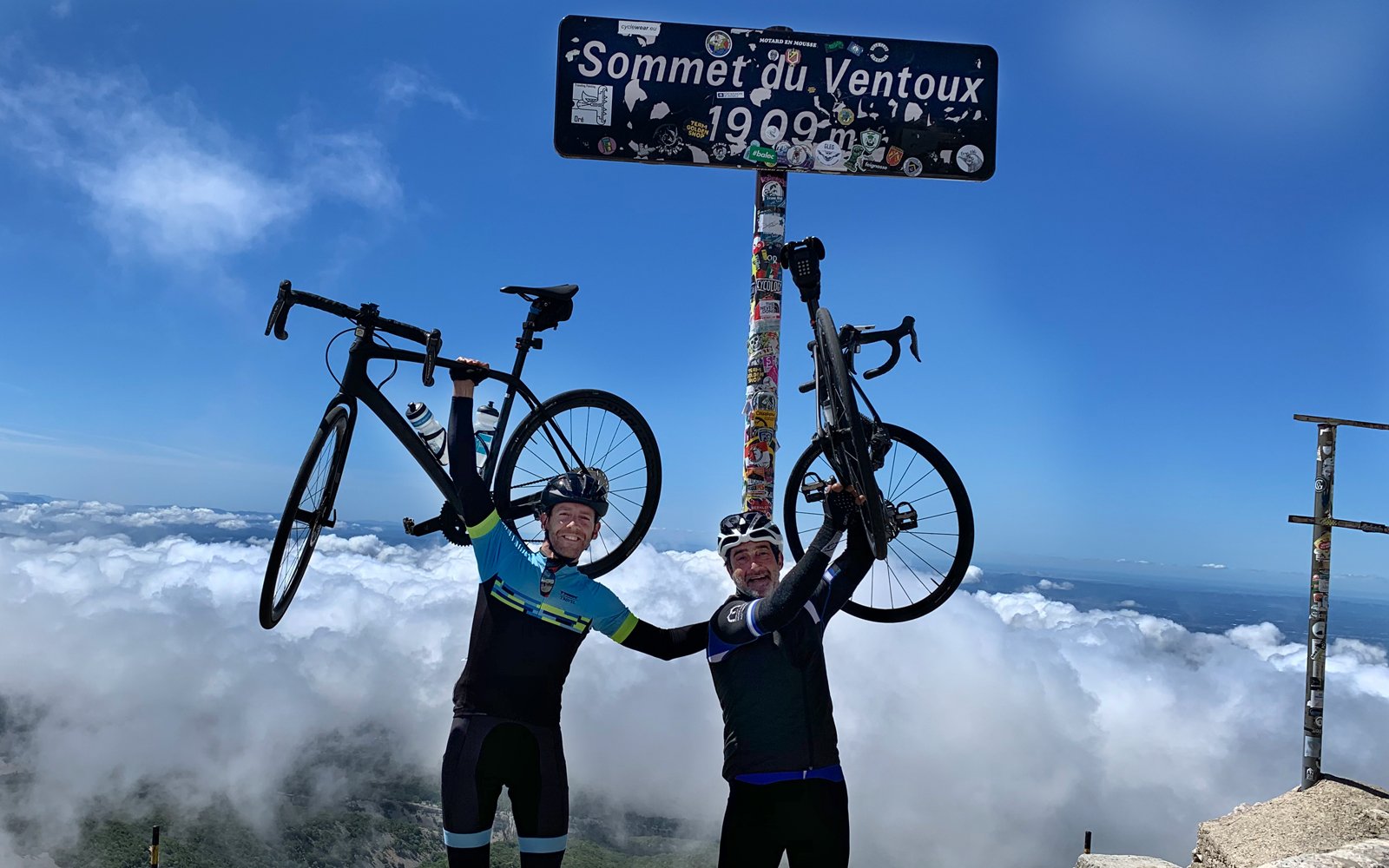 Two cyclists hoisting their bikes below the Mont Ventoux sign