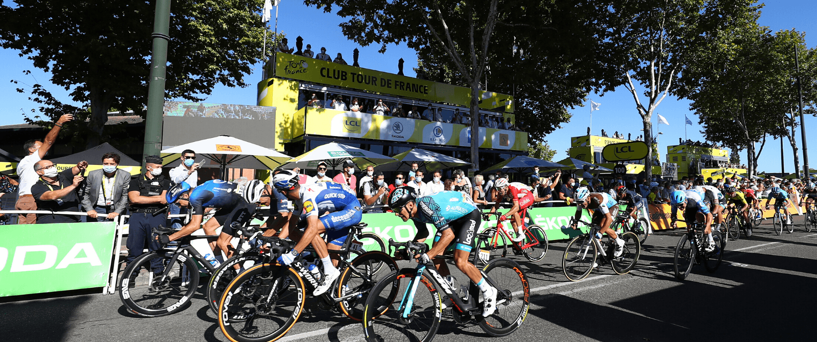 Cyclists sprinting in front of the Club Tour de France stall