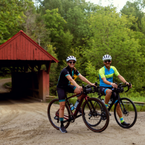 Two cyclists standing in Vermont with a famous covered bridge behind them