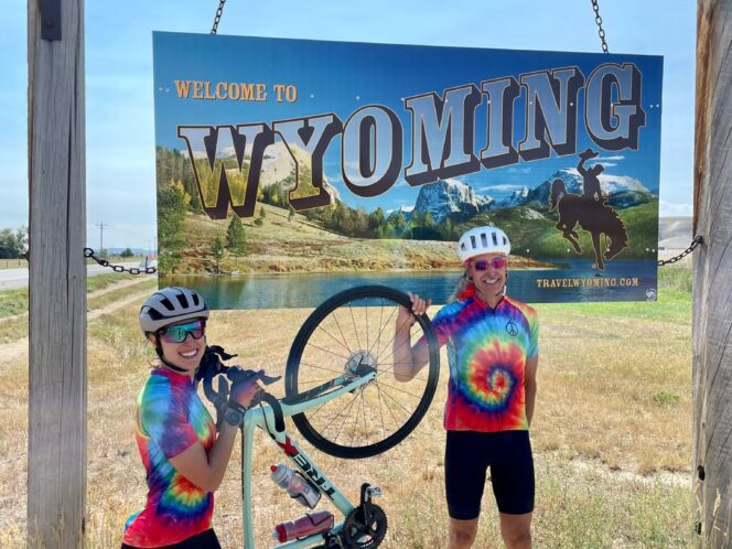 Two people standing with one bike under the "Welcome to Wyoming" state sign