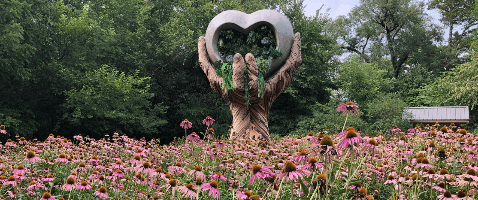 Large hand holding heart sculpture in field of wildflowers