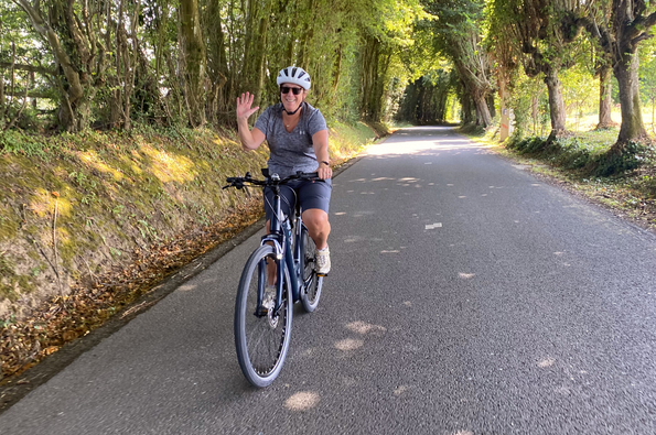 Ebike rider on tree lined avenue waves and smiles for the camera