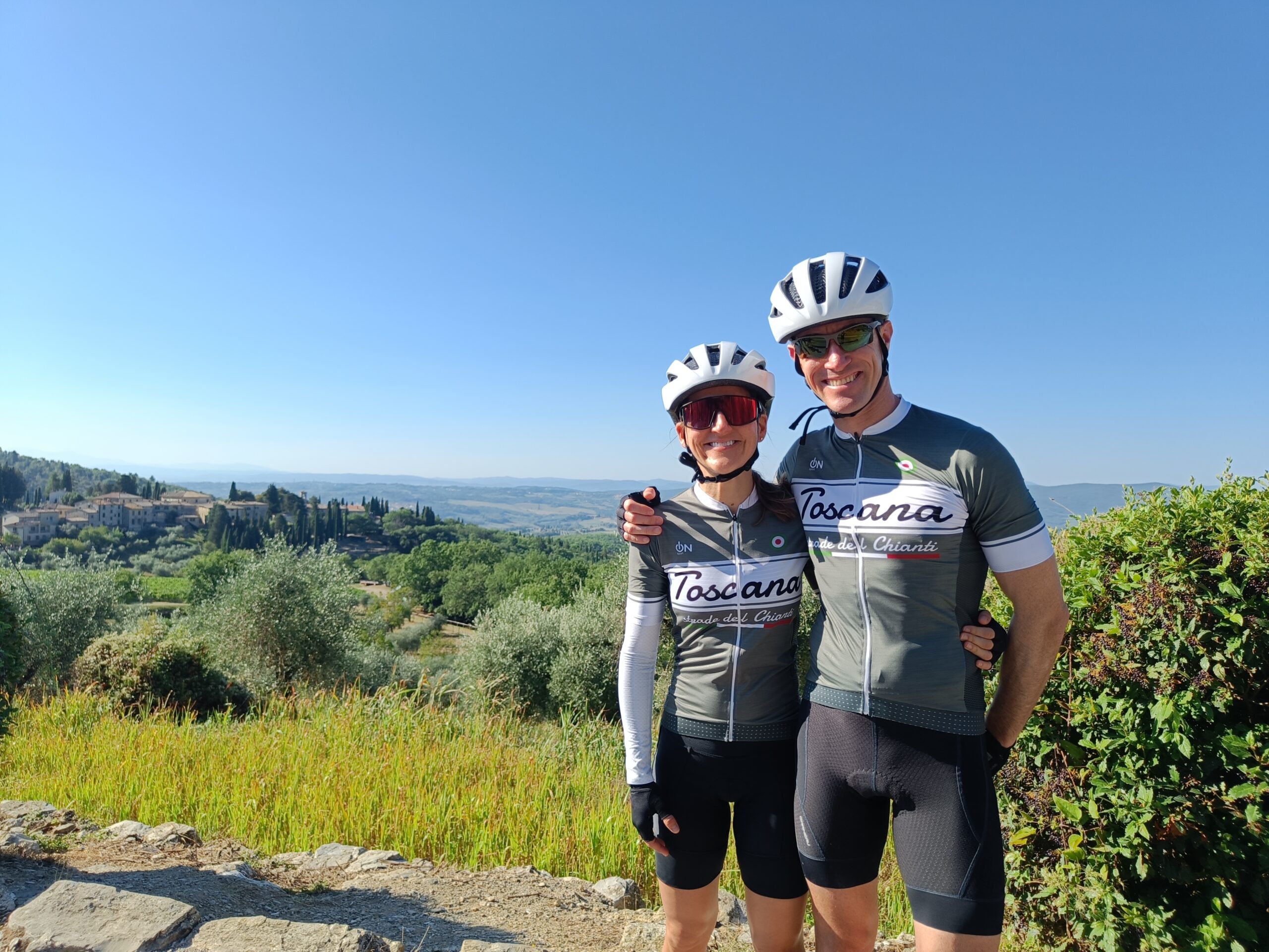 A cyclist couple wearing Toscana jerseys in front of a landscape