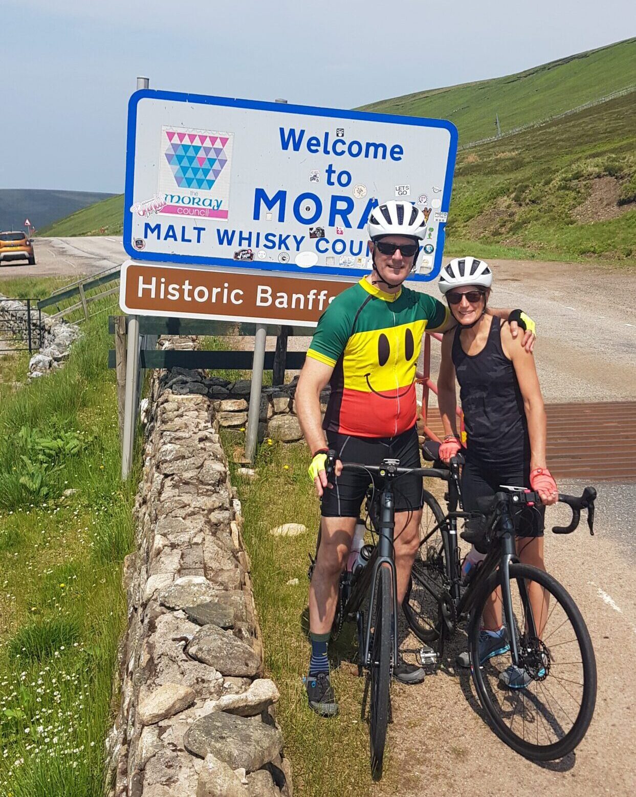 Two cyclists in front of a Malt Whisky Country sign