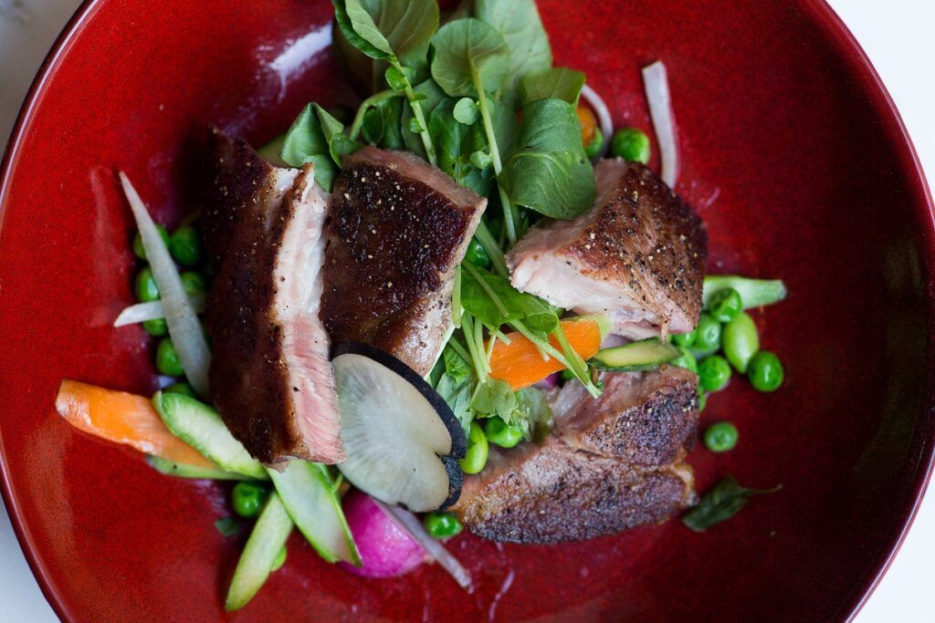 Beautifully arranged seafood entree with peas, greens and a flower on a dark red plate