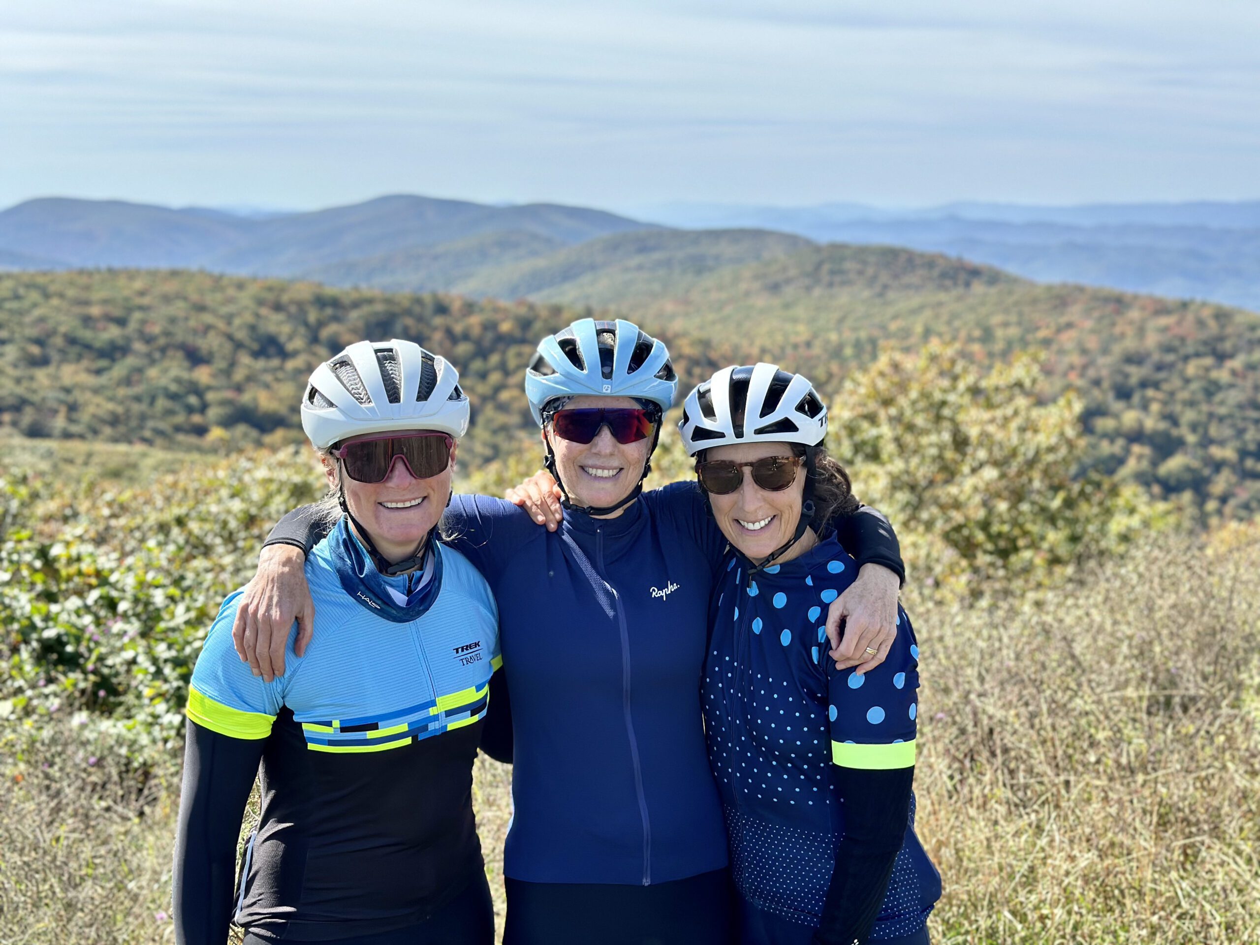 Three women cyclists standing at summit with Blue Ridge Mountains in the distance.