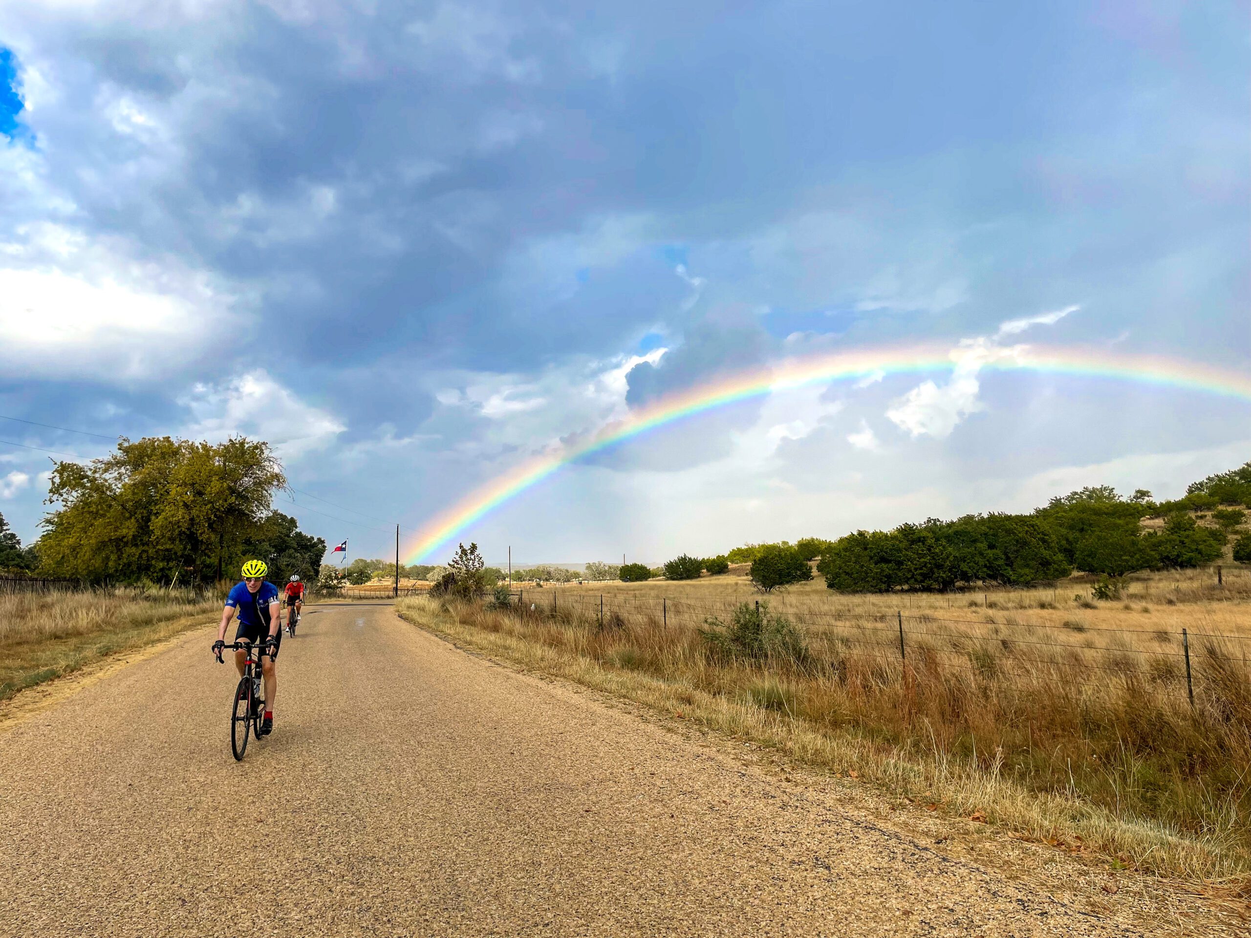person riding their bike on a gravel road with a beautiful rainbow in the background