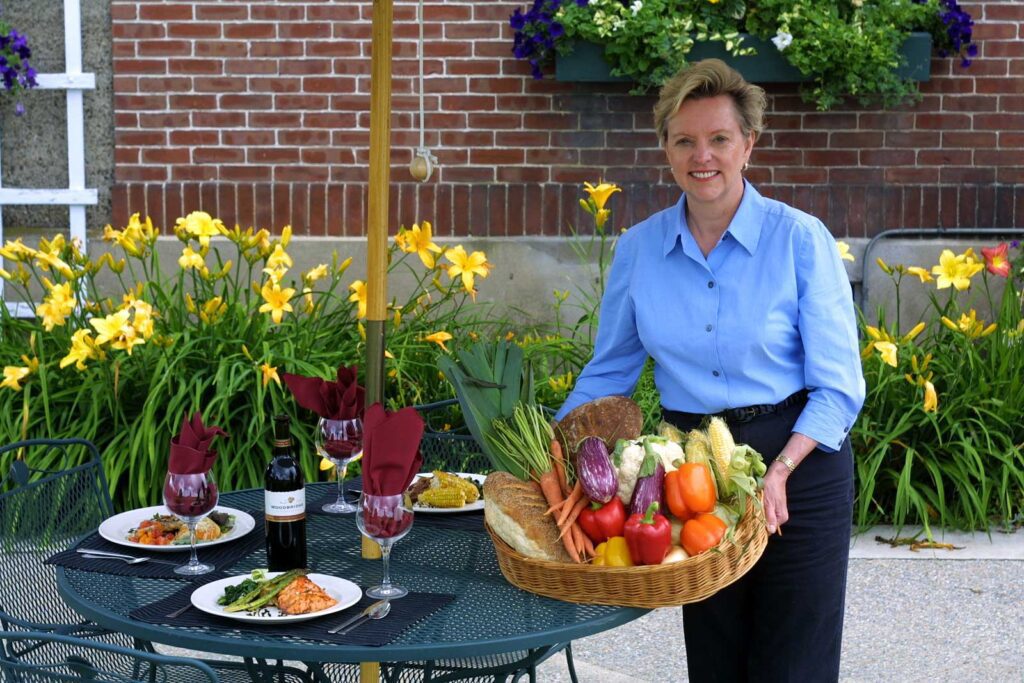 Woman with fresh produce in a basket with outdoor dinner setting.