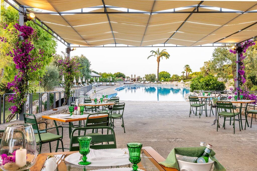 Outdoor patio with tables and chairs, with large pool and palm trees