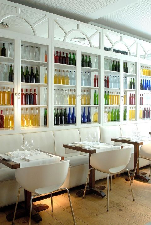 Rows of set tables with a wall of shelves filled with colorful bottles.