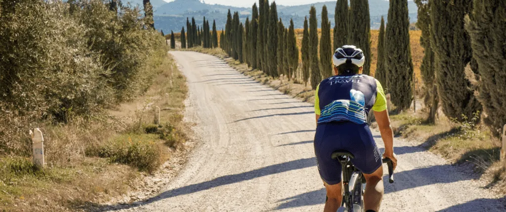 Rear view of lone cyclist on gravel road with cyprus trees