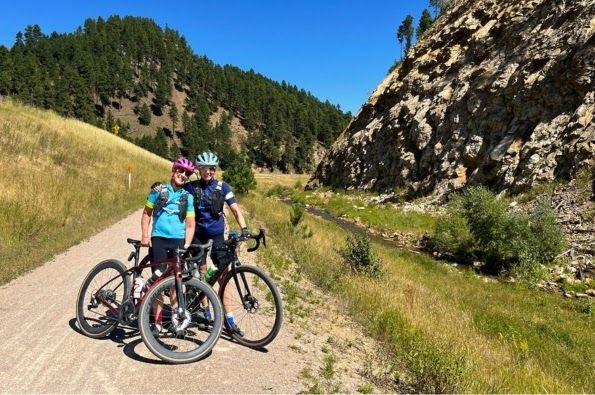 Two cyclists on a gravel path with hills in the background