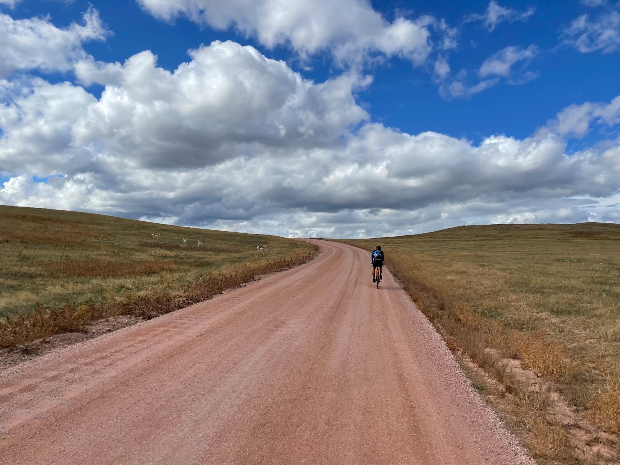 Cyclist on dirt road under blue sky with white puffy clouds